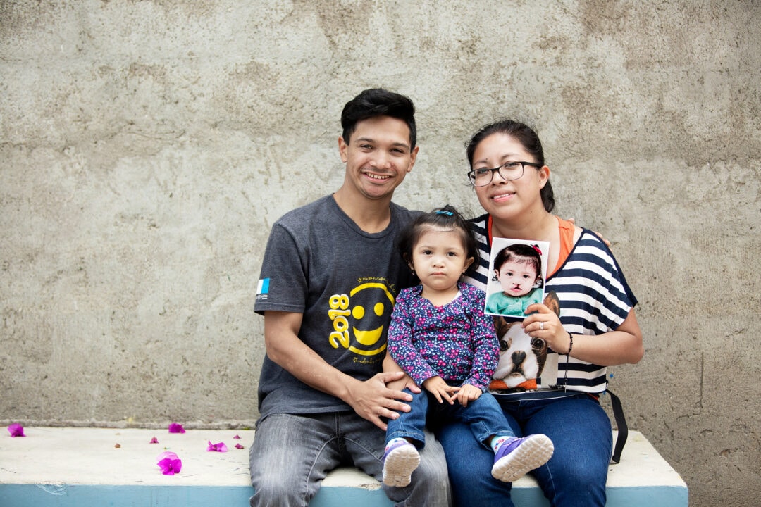 Fatima with her parents, holding a photo of herself before cleft surgery. Photo: Carlos Rueda