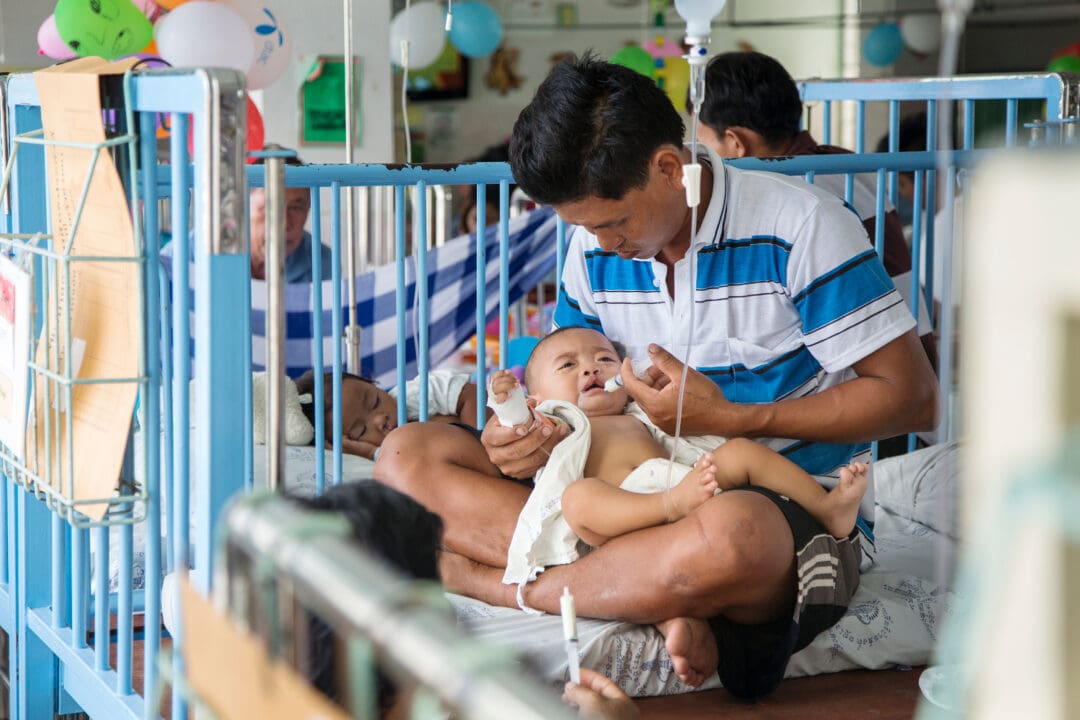 Baby boy with father feeding in ward after surgery.