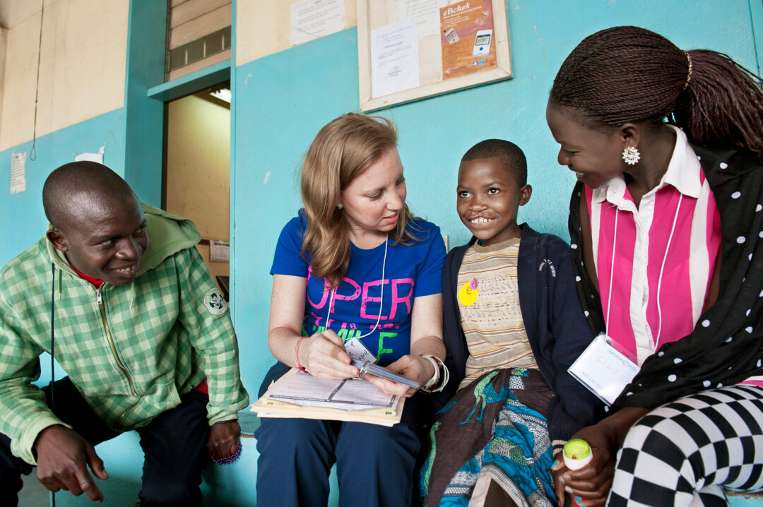 Mina's dad, Jangiya, looks on as his daughter smiles wide as she sits between volunteer speech pathologist Valerie Dorfman of the U.S. and translator Finess of Malawi. Photo: Margherita Mirabella.