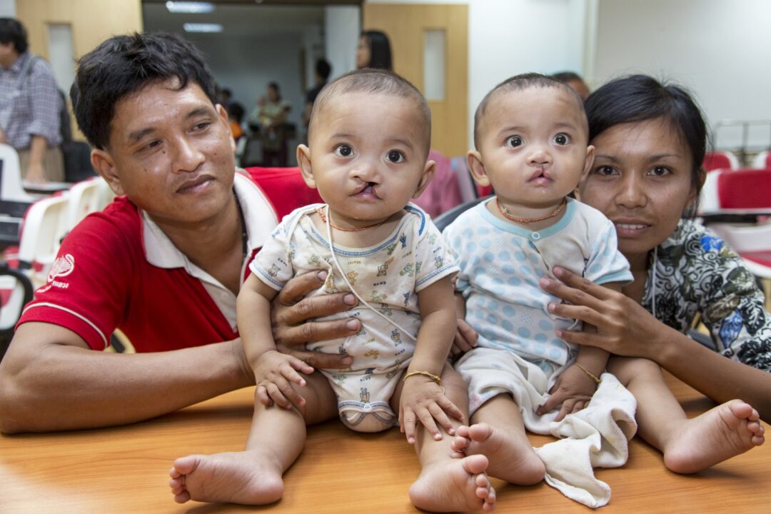 Manus, left, and Wanna hold their twin sons, Ou and Lak, centre, as they await their comprehensive health evaluations during an Operation Smile medical programme in Thailand. Photo: Peter Stuckings.